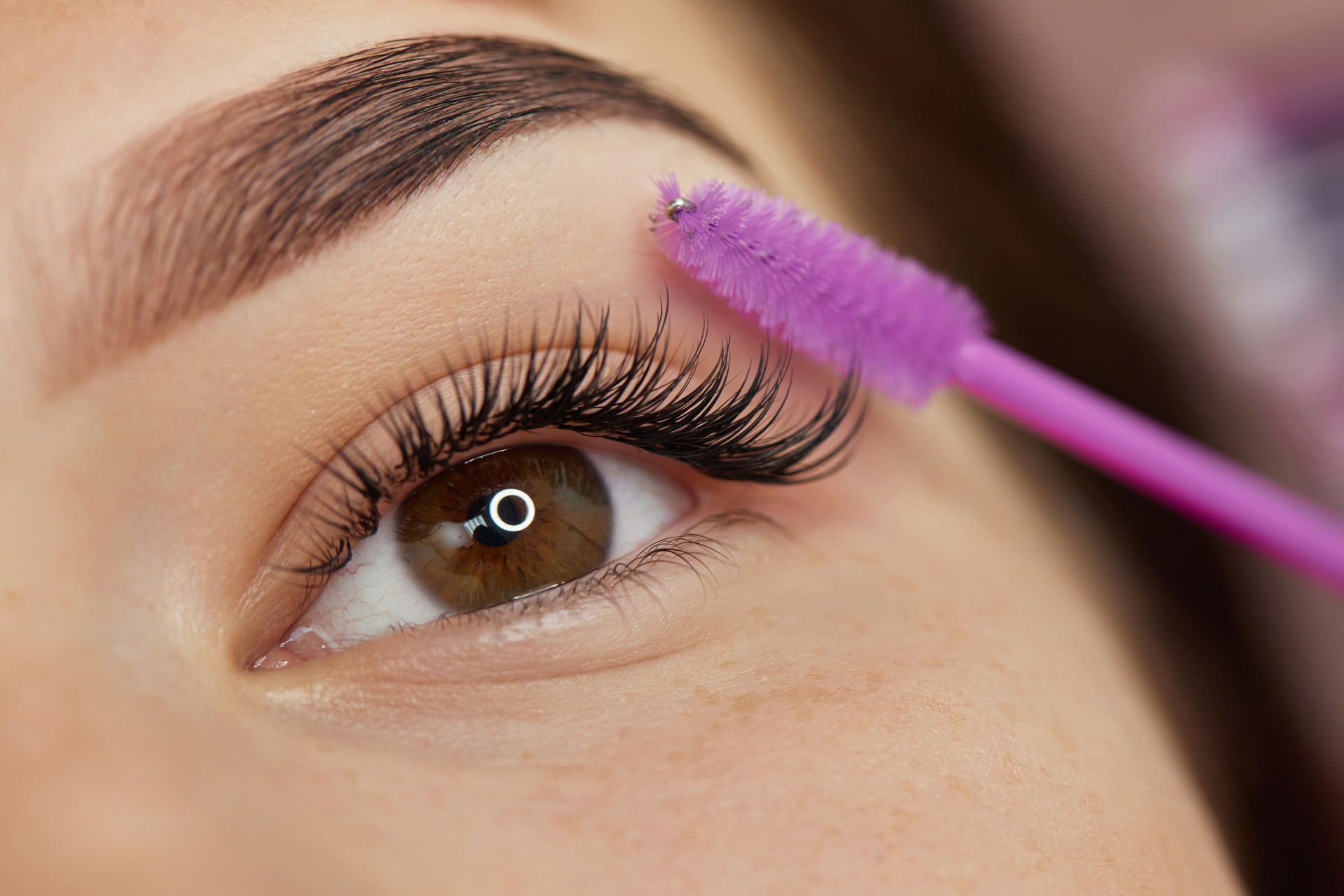 cosmetologist combs eyelashes of client after eyelash extension procedure